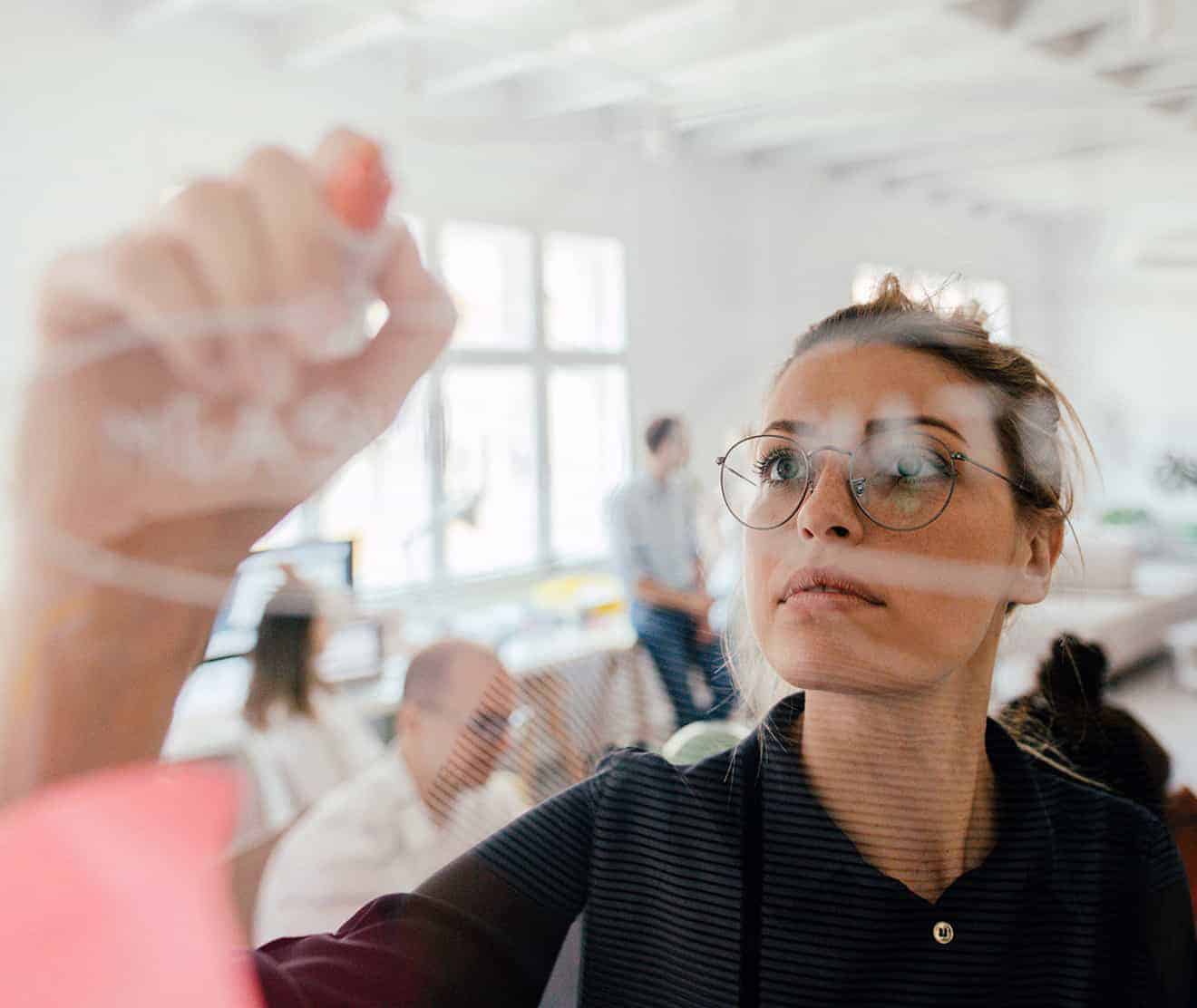 Woman attentively writing on transparent whiteboard